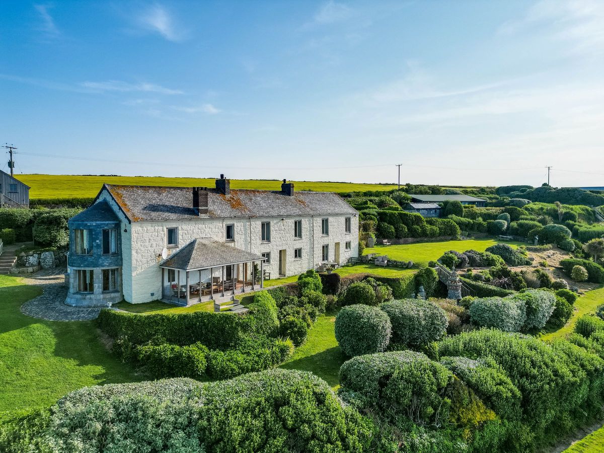 A stone house with a large garden with a variety of bushes and outbuildings to the end of the garden