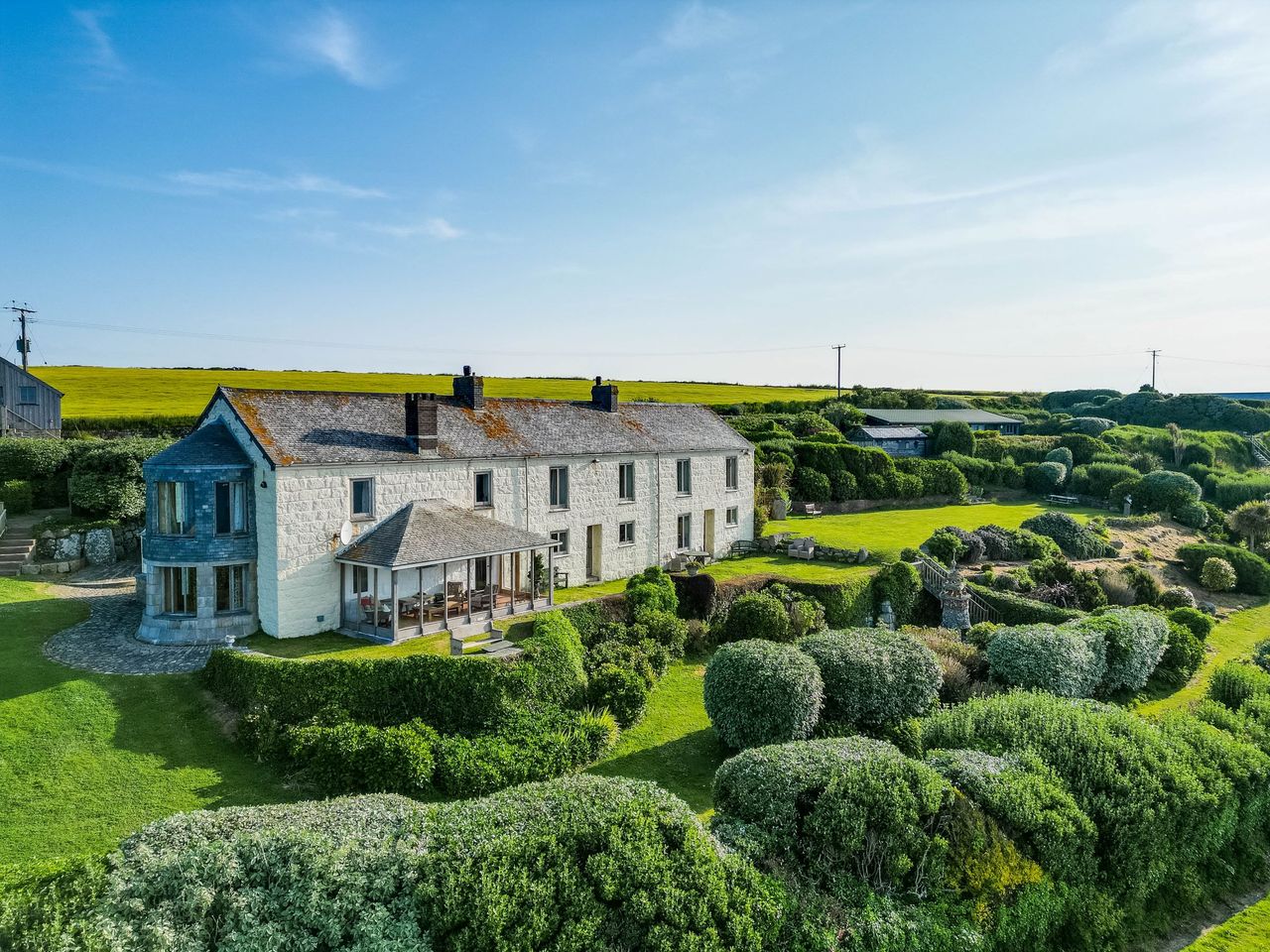A stone house with a large garden with a variety of bushes and outbuildings to the end of the garden