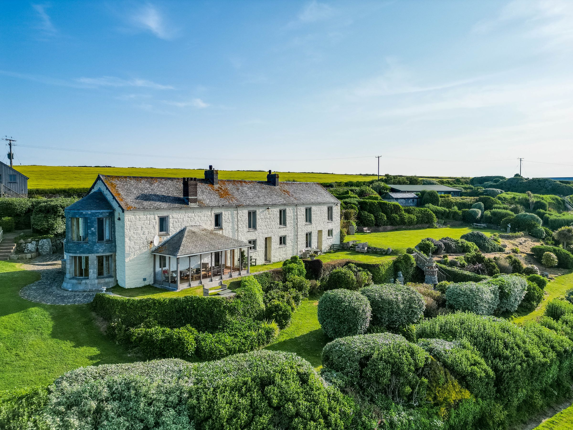 A stone house with a large garden with a variety of bushes and outbuildings to the end of the garden