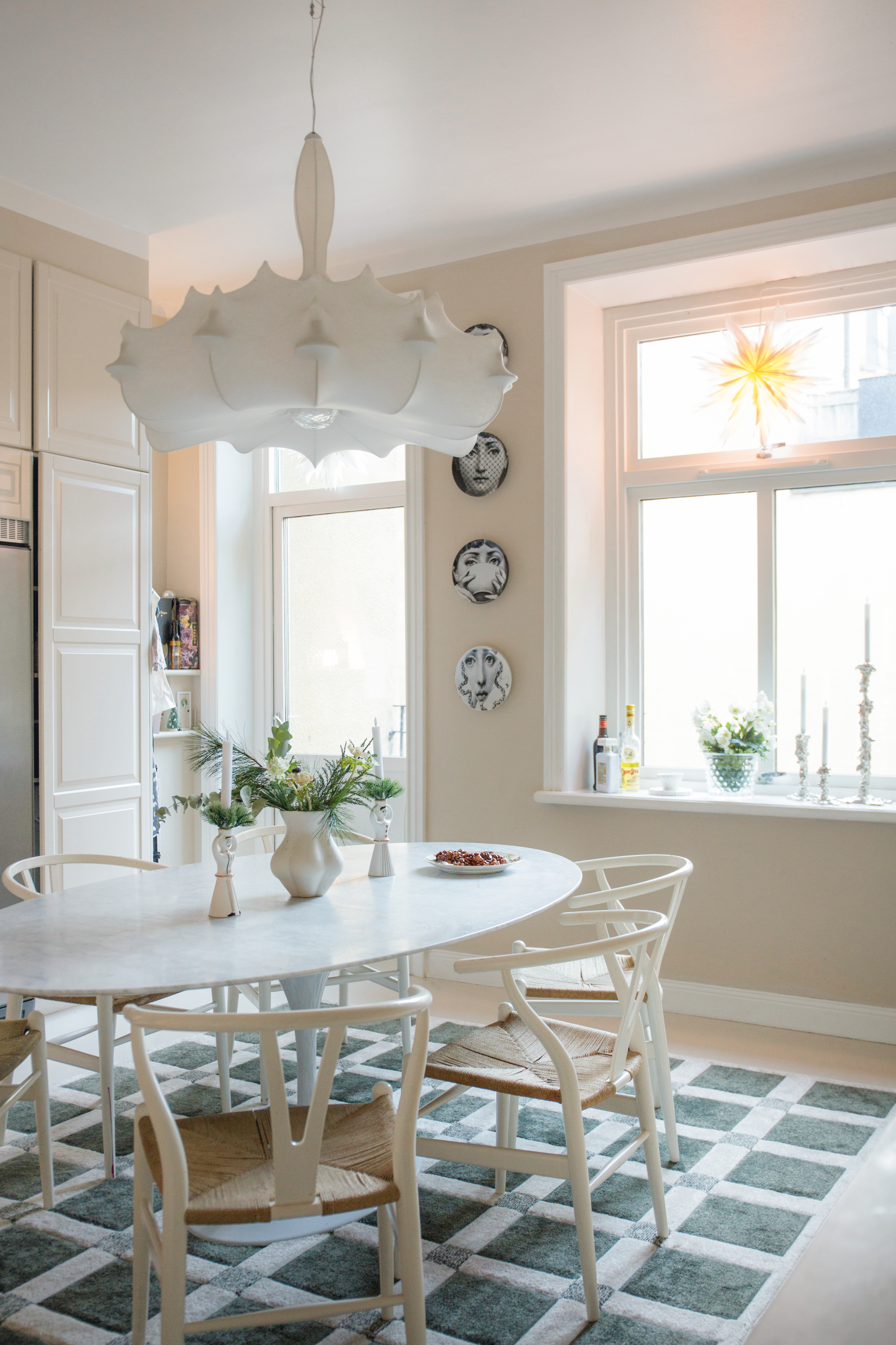 Cream kitchen with white table, white chairs, green and white rug and a white pendant light