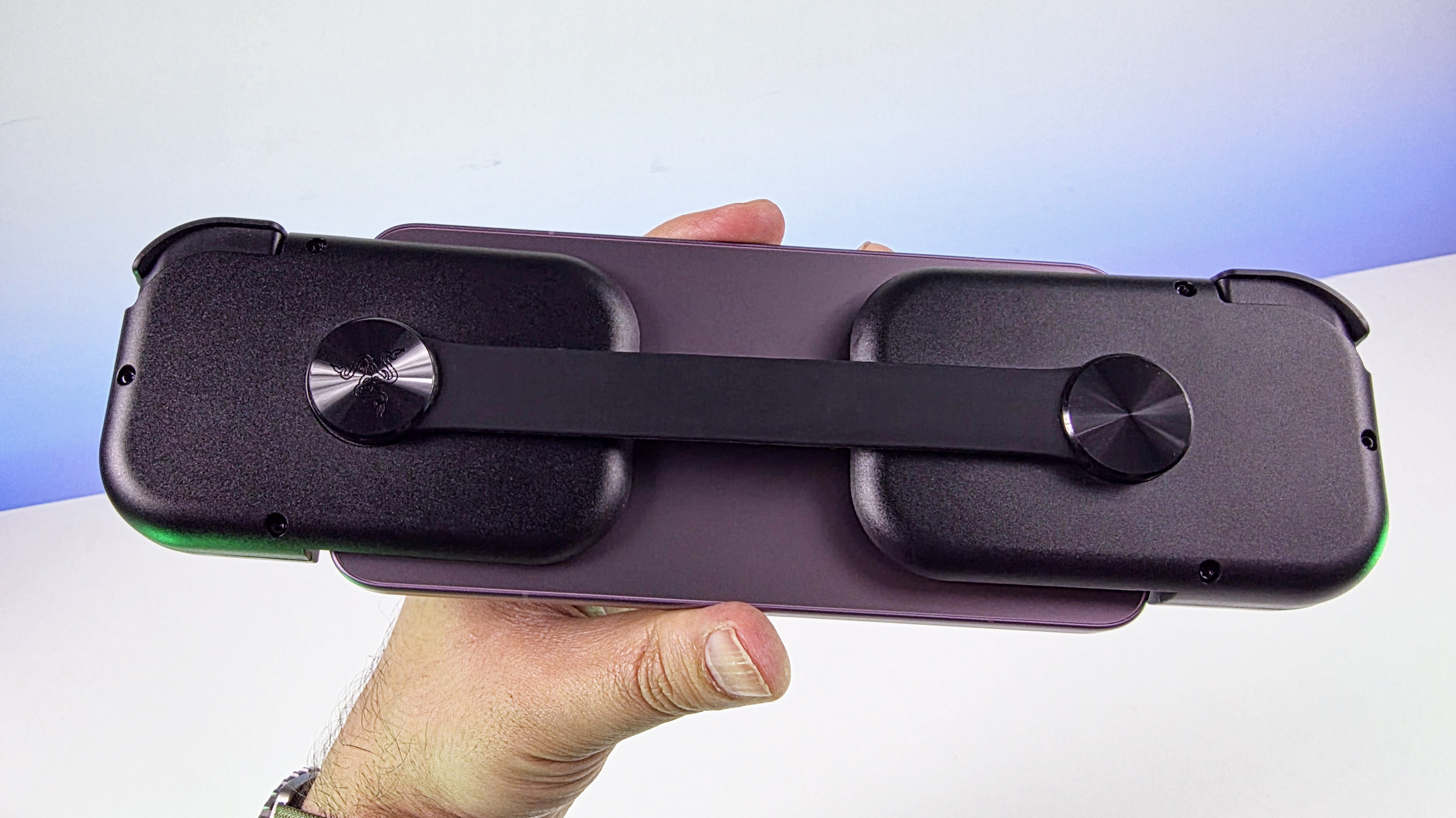 Hand holding the back of a smartphone attached to the Razer Prio controller, highlighting the flexible rear strap connecting the two handgrips.