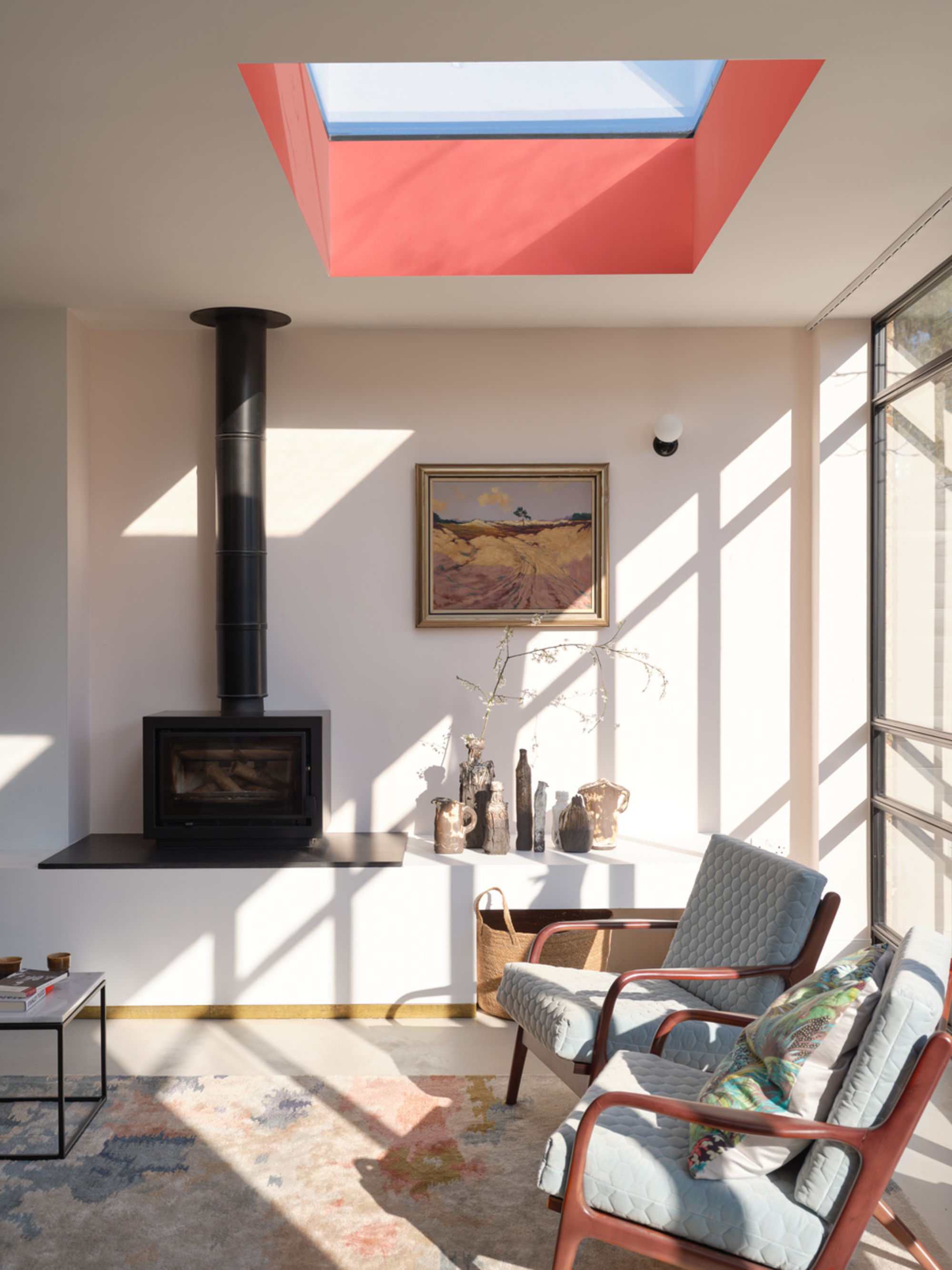 A living room with off white walls, a wood burner, and a skylight with the recessed ceiling painted red