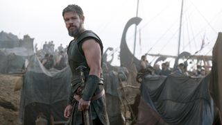 Matt Damon's Odysseus looking over his left shoulder with some ships in the background in The Odyssey