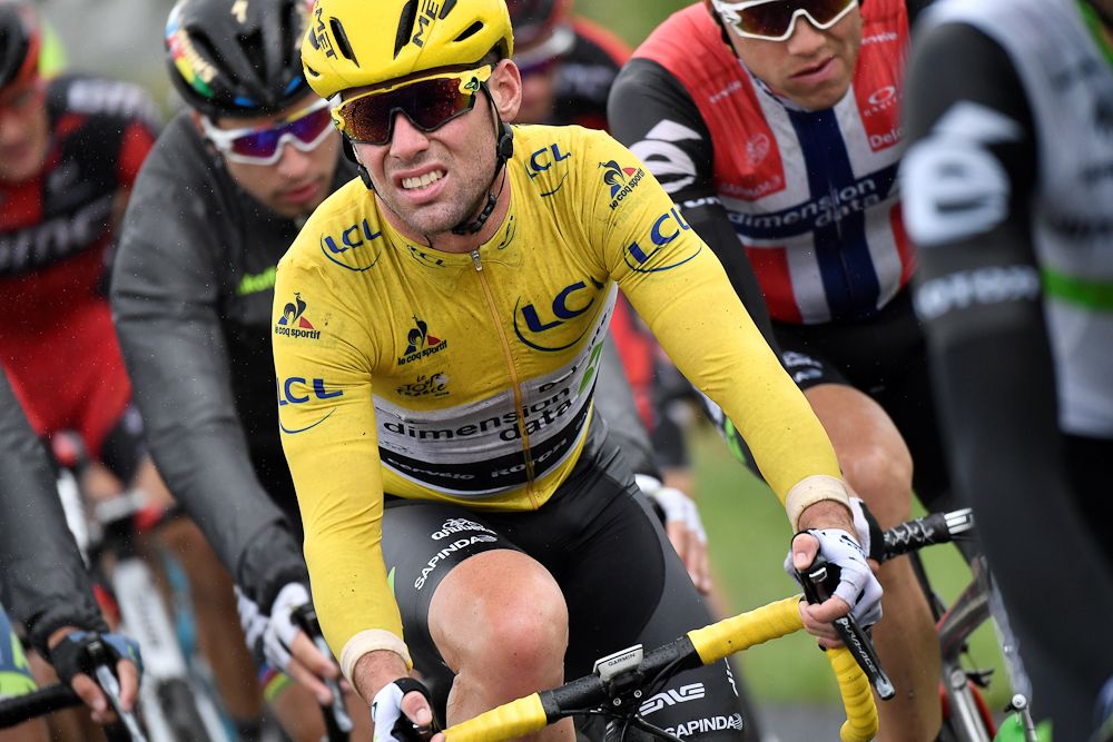 Mark Cavendish (C), wearing the overall leader's yellow jersey, grimaces as he rides in the pack during the 183 km second stage of the 103rd edition of the Tour de France