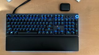Bästa gamingtangentbord: Ett Razer Huntsman V2 Analog-tangentbord ligger på ett träfärgat skrivbord, med tangenterna upplysta i blått.