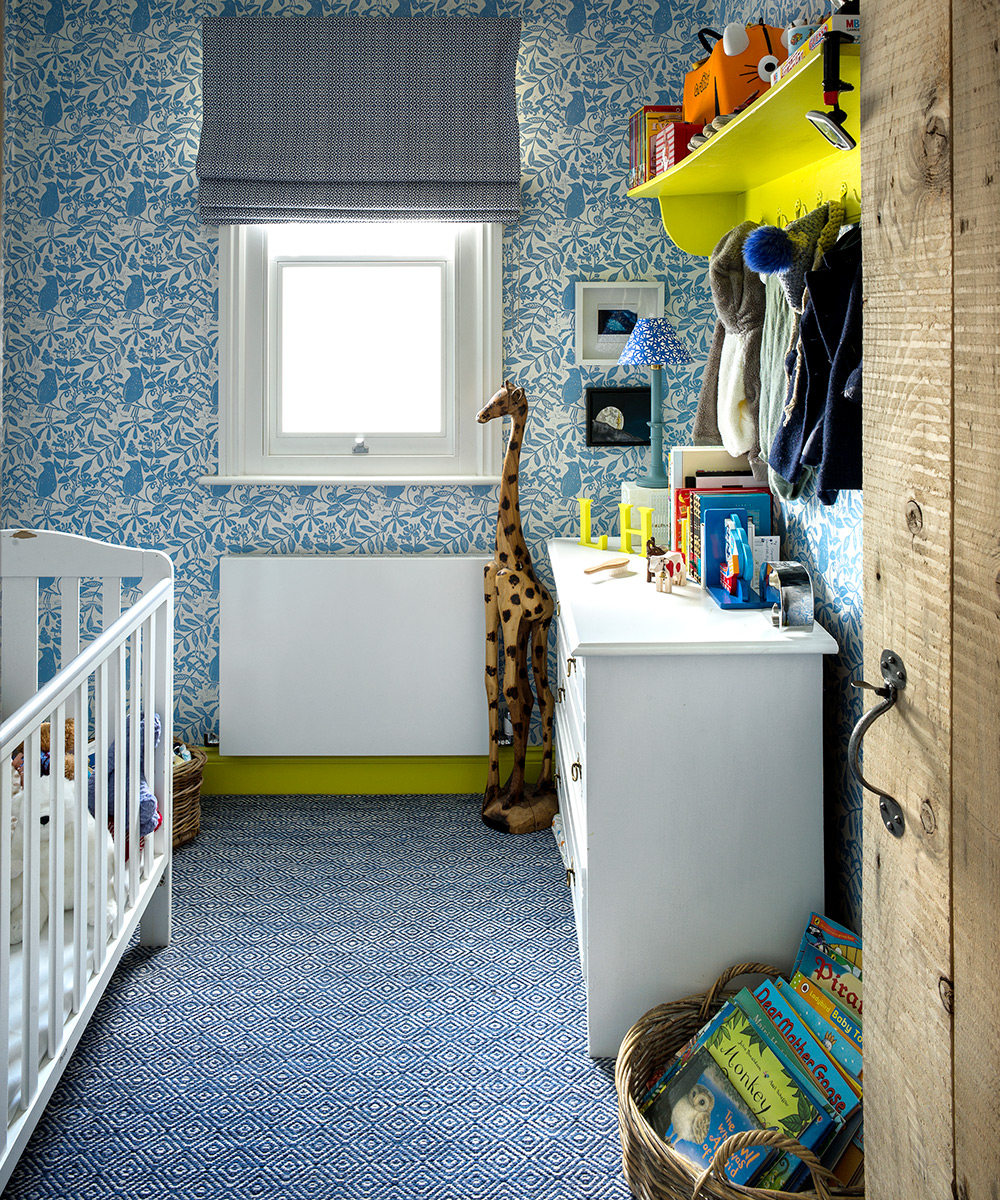 Decorating a nursery for kids to grow in, shown here with blue patterned wallpaper and rug and white furniture.