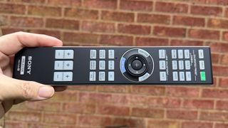 Sony Bravia Projector 9 home cinema projector remote control held in hand against brick wall