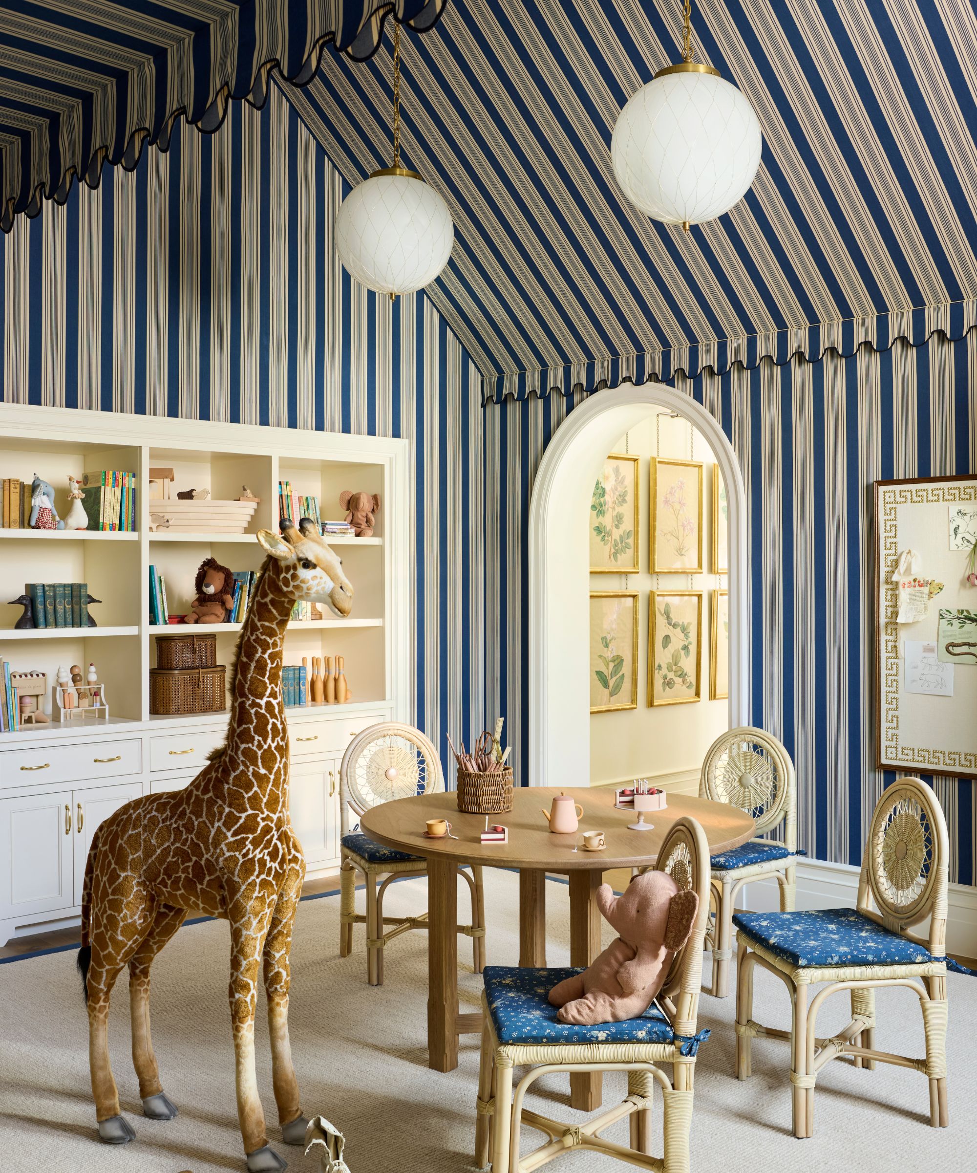 a blue striped tent-like playroom with scalloped wall trim, globe lights an arched door, childrens furniture and a large giraffe toy