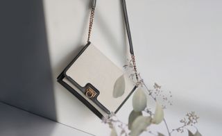 View of Salvatore Ferragamo’s Trifolio flap bag in a space with light coloured walls and flowers. The bag is black and white with a gold closure and chains in the strap