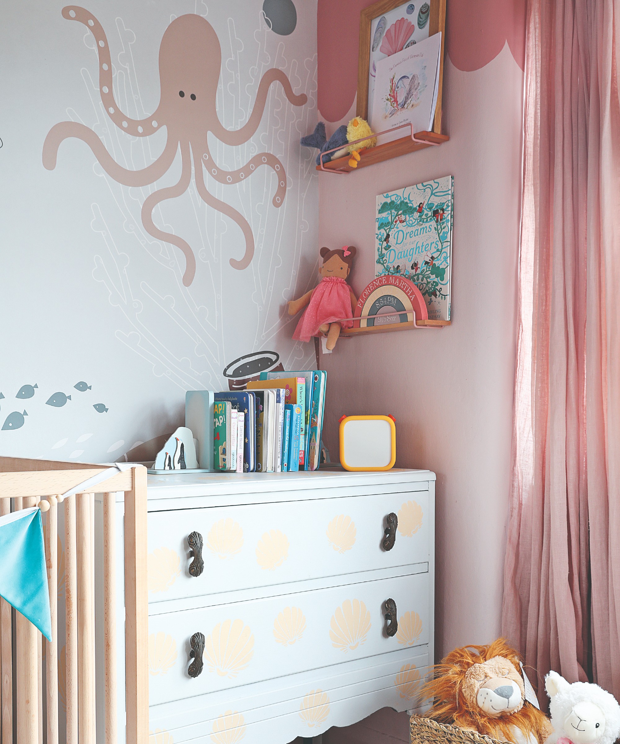 A pastel-coloured nursery with a sea world-inpired wallpaper and painted chest of drawers