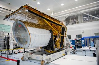 The Euclid spacecraft with large white cylinder and gold and silver colored foil outer rectangular frame, pictured inside a lab where people are wearing laboratory coats and hair nets.