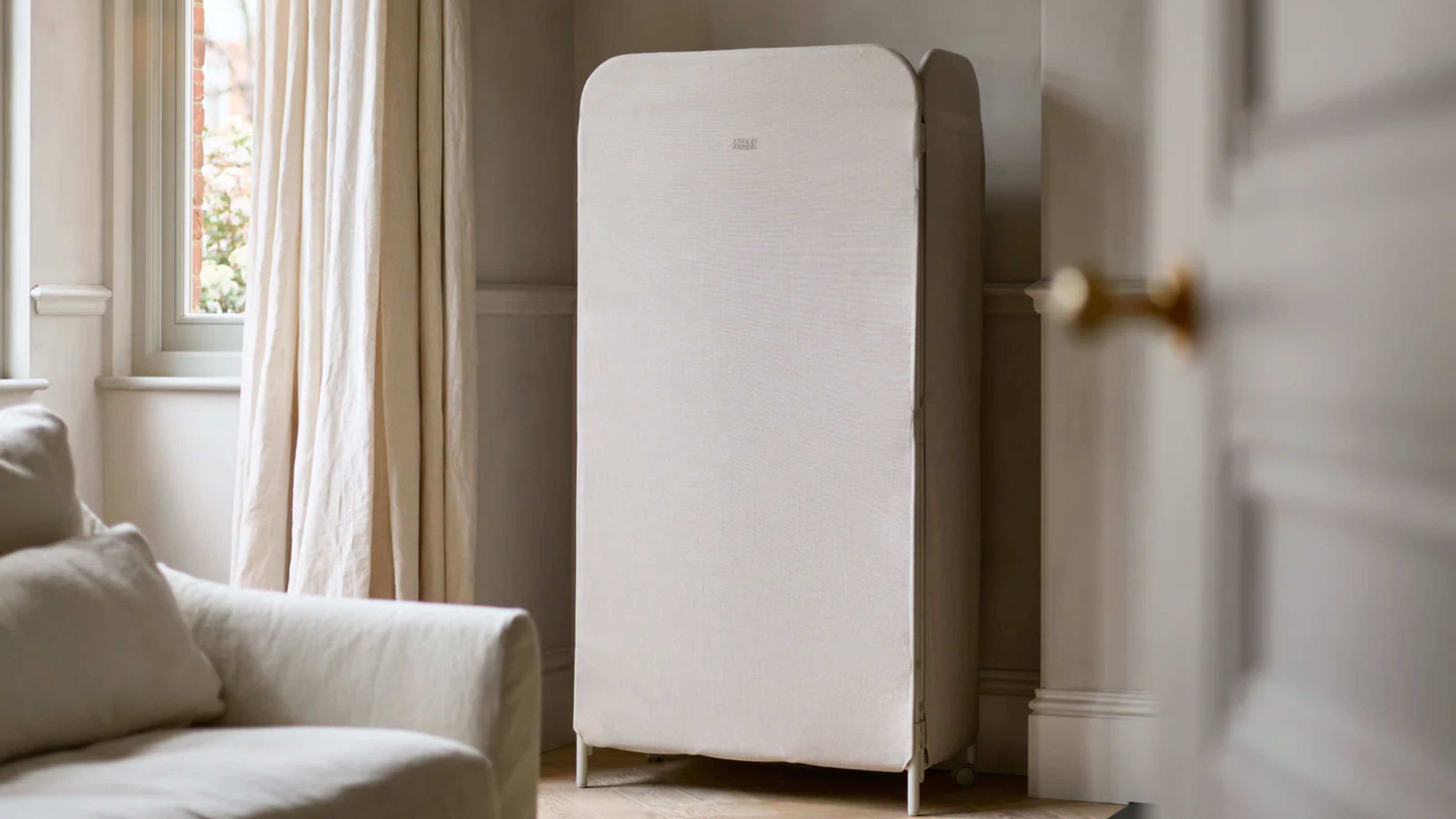 Joseph Joseph eclipse drying rack in a white living room with white couch, large windows with white curtains, and open white door.