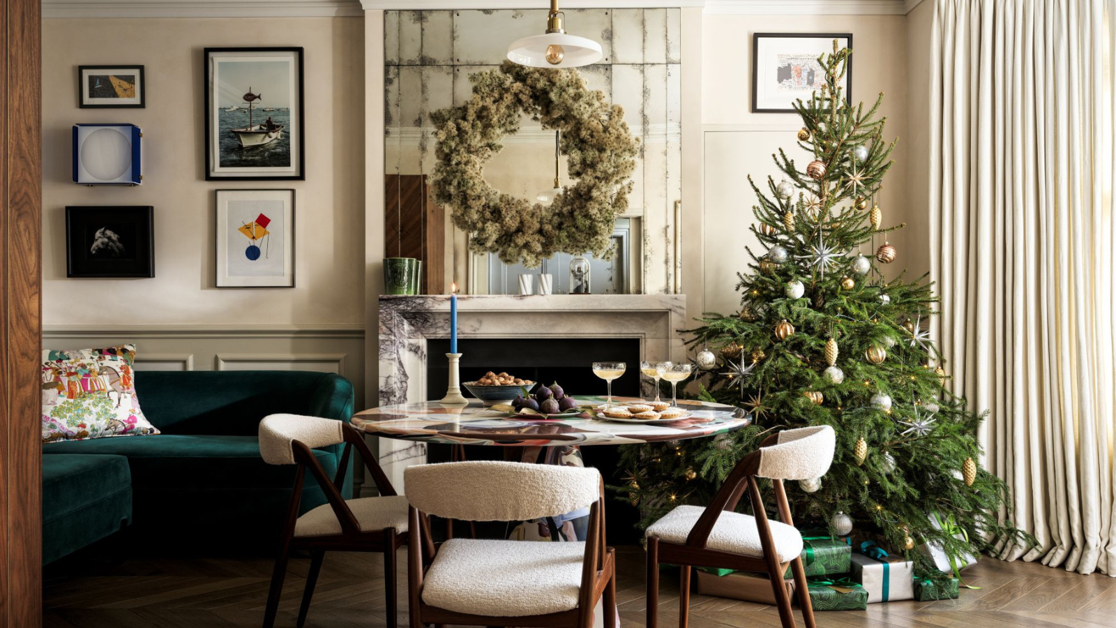 a dining room with a round dining table and three dining chairs, a Christmas tree, and a fireplace with a large wreath above it