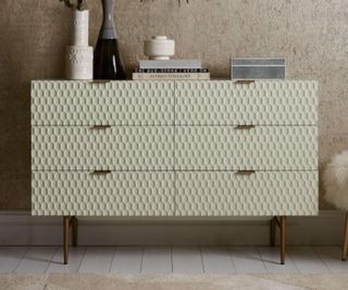 West Elm dresser with trinkets on top. Set on carpeted floor, against a plain bedroom wall.