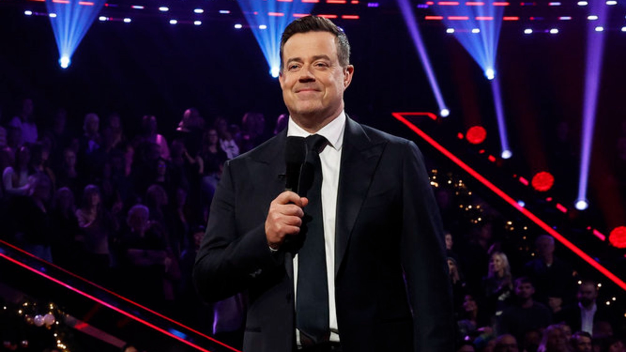 Carson Daly holding a microphone on The Voice.