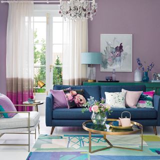 A living room with purple walls, a blue sofa and a chandelier