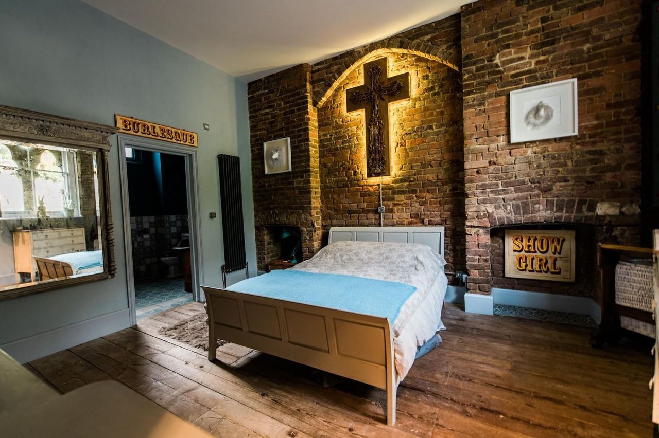A bed with a cross on the wall above the bed and an en suite bathroom with wooden flooring