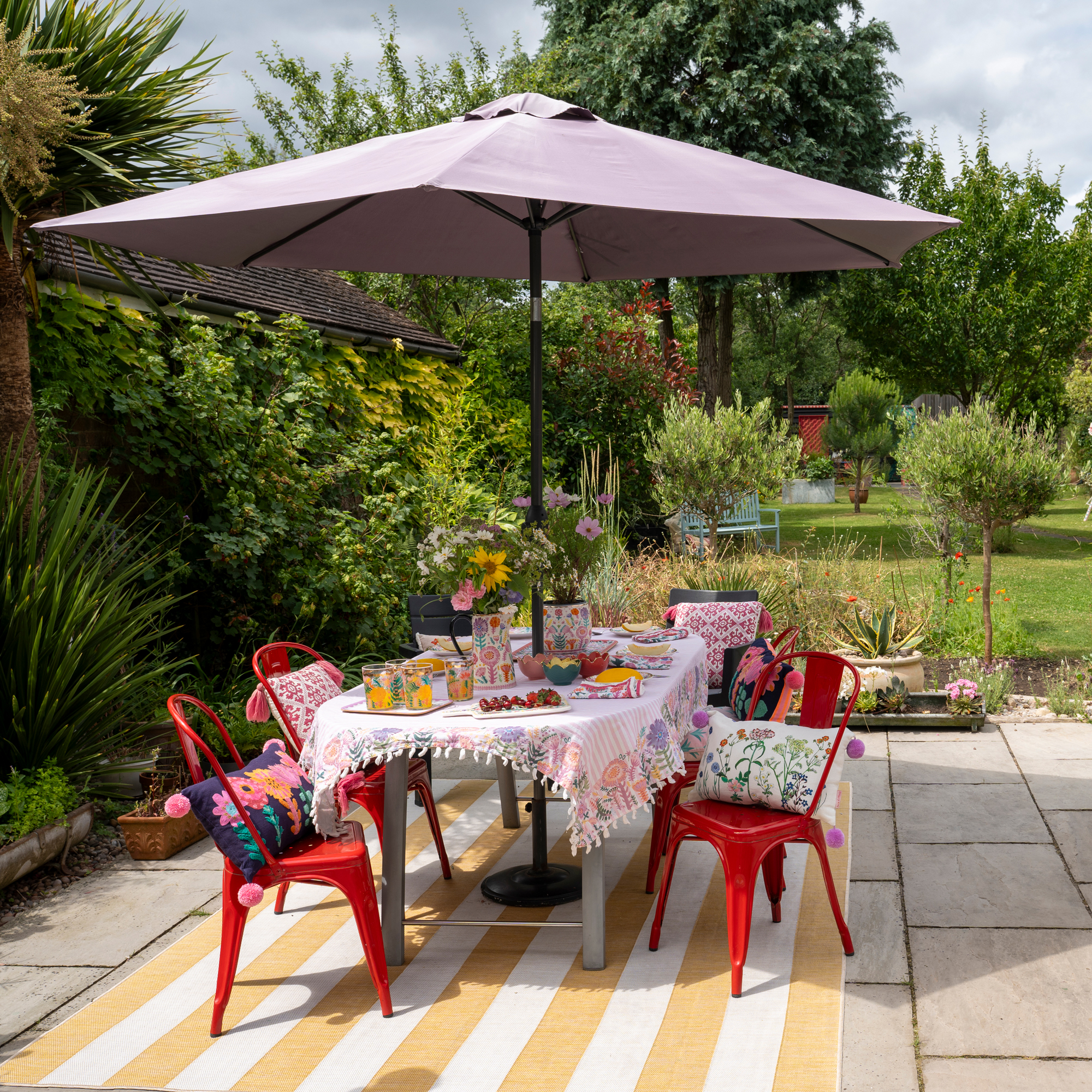 garden with a dining table and red metal chairs and parasol with a yellow and white striped rug 