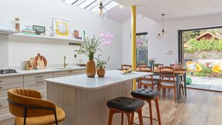 open plan kitchen diner with white walls and units, kitchen island with bar stools, dining table and chairs, rooflights, yellow structural column and bi-fold patio doors