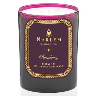 A candle in a pink tinted container with gold decoration on the label
