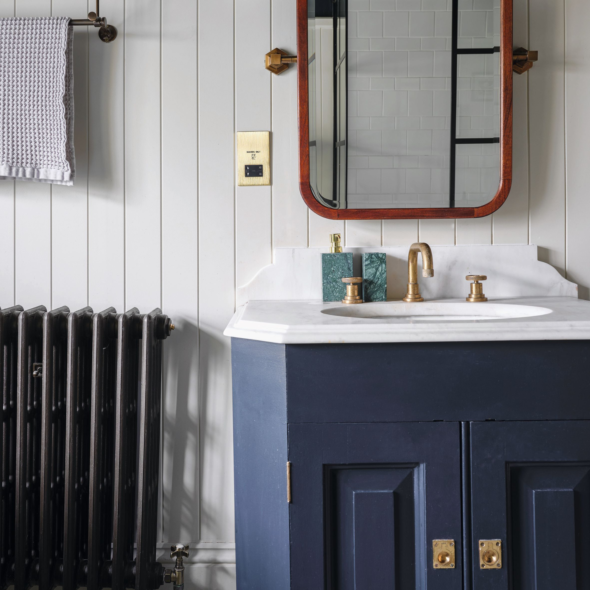 Handbasin with white and grey marbled top, blue vanity unit, wood panelled wall and original cast iron radiator