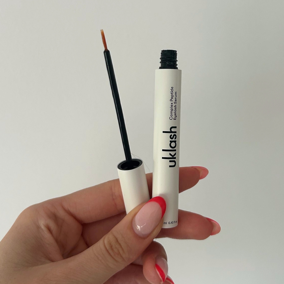 Hand holding empty white tube of UKLash Complex Peptide Lash Growth Serum