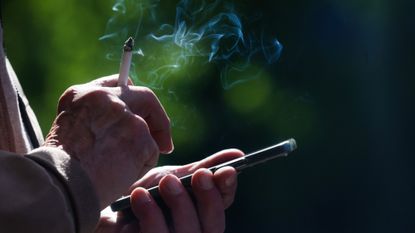 A man smokes a cigarette while using his cell phone. 