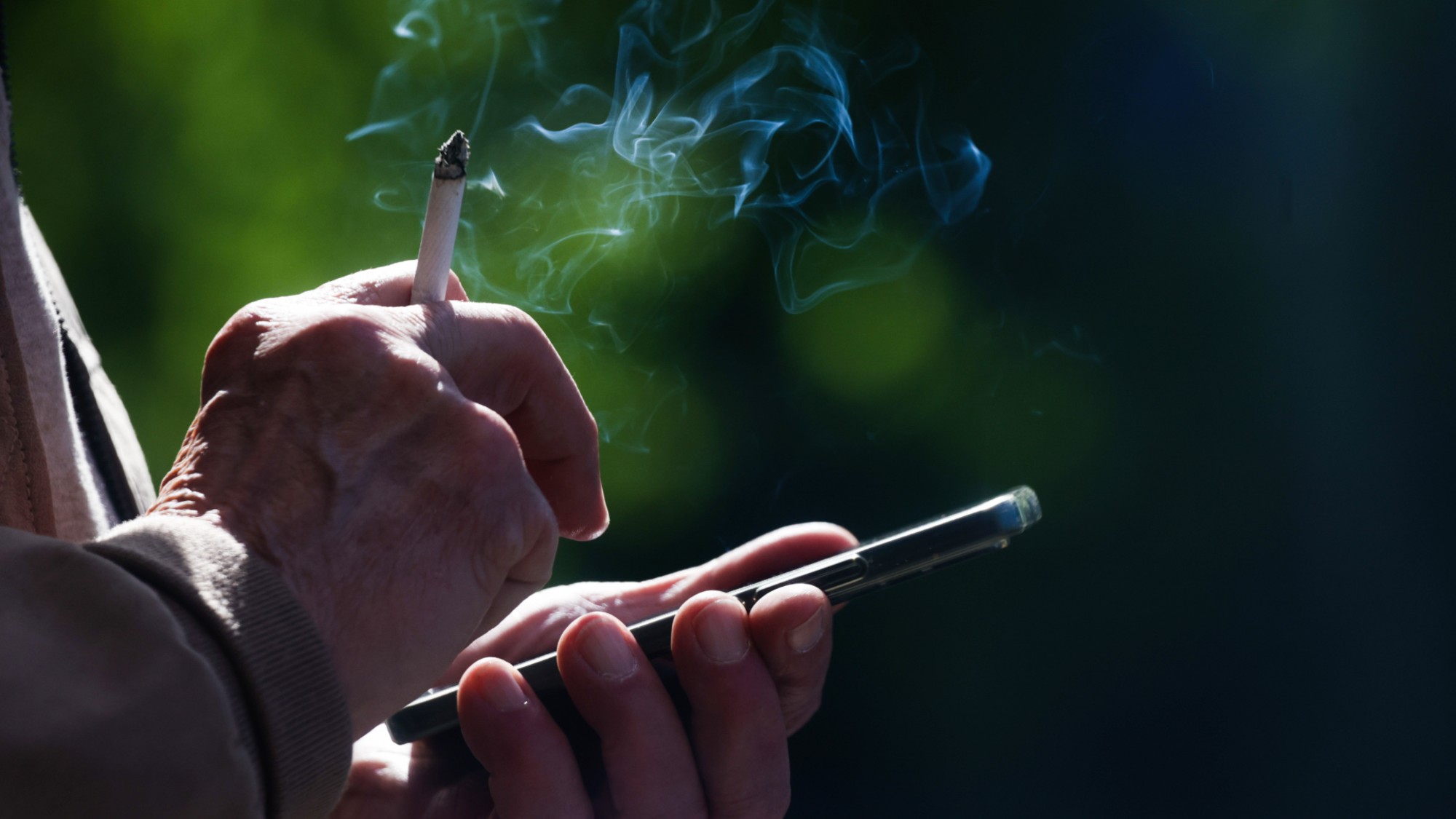 A man smokes a cigarette while using his cell phone. 