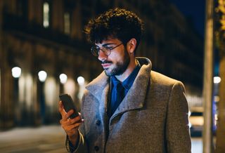 A person using their smartphone in a street at night.