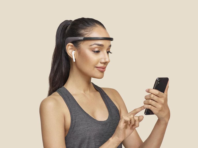 Woman wearing Muse 2 meditation headband uses touchphone. 