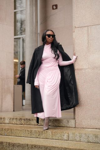 A Milan Fashion Week attendee wears a black maxi coat with a pink dress