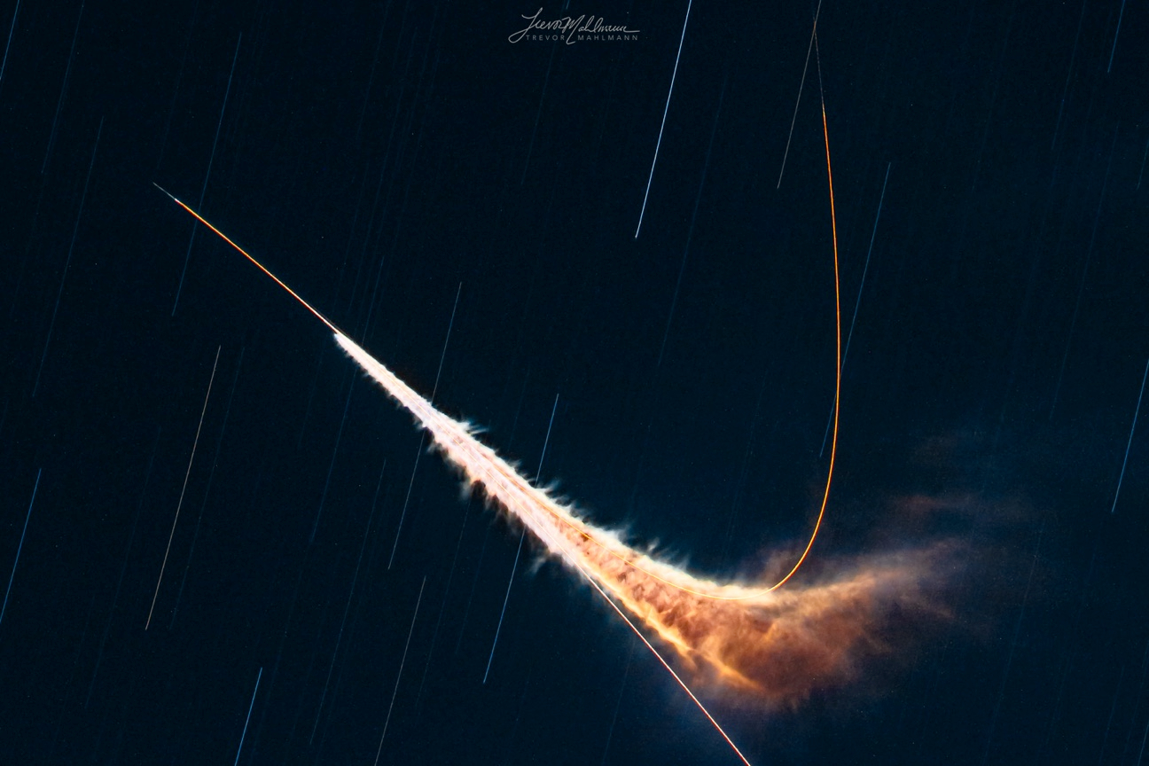 A rich, deep, dark blue sky is streaked with the falling lines of faint stars. Against their descent, a bright orange streak shoots from right of bottom center, arrowing diagonally upward, left, as a blistering white cloud rips from the sure line to form a second, shooting first with white and orange mist, then emerging at once to an orange determination rooting upward, nearly reaching the top.