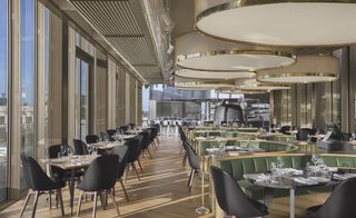 W Hotel dining room with large windows, round ceiling lights and horseshoe shaped green banquette seating
