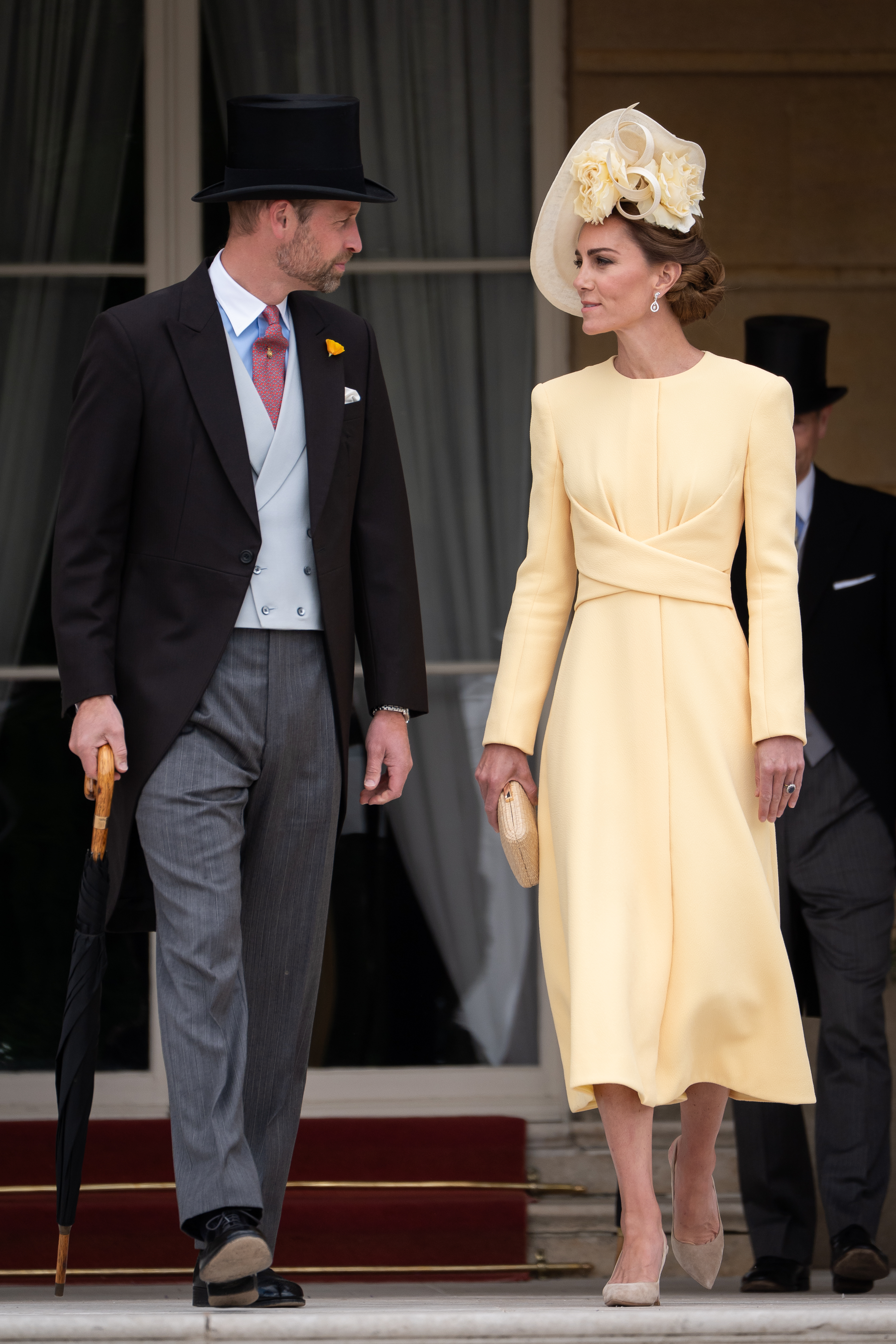 Kate Middleton wearing a yellow dress walking next to Prince William, wearing a top hat and suit