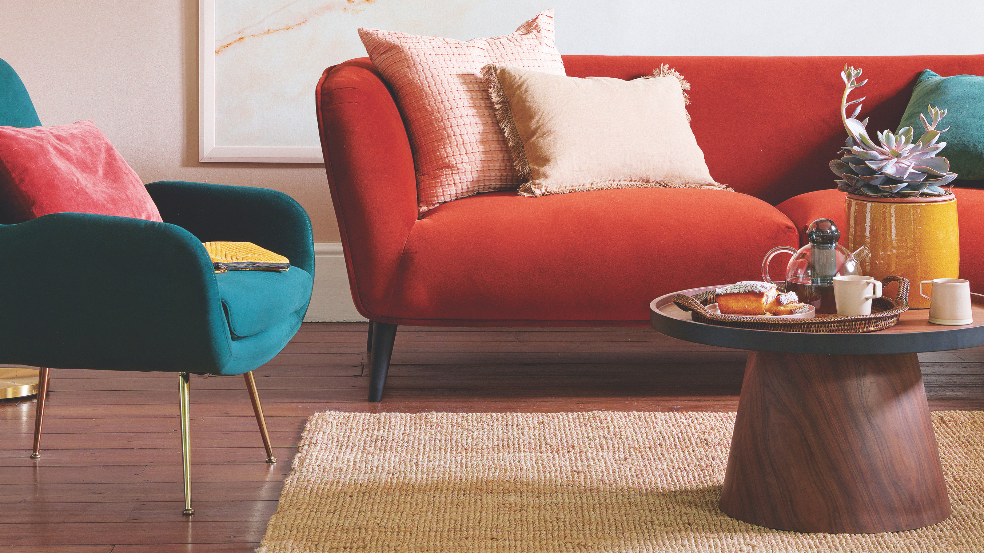 Living room with pink wall and framed wallpapered panel, wooden floor, red sofa and green armchair.