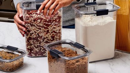 A set of Rubbermaid Brilliance containers on a marble kitchen counter filled with dried pantry goods