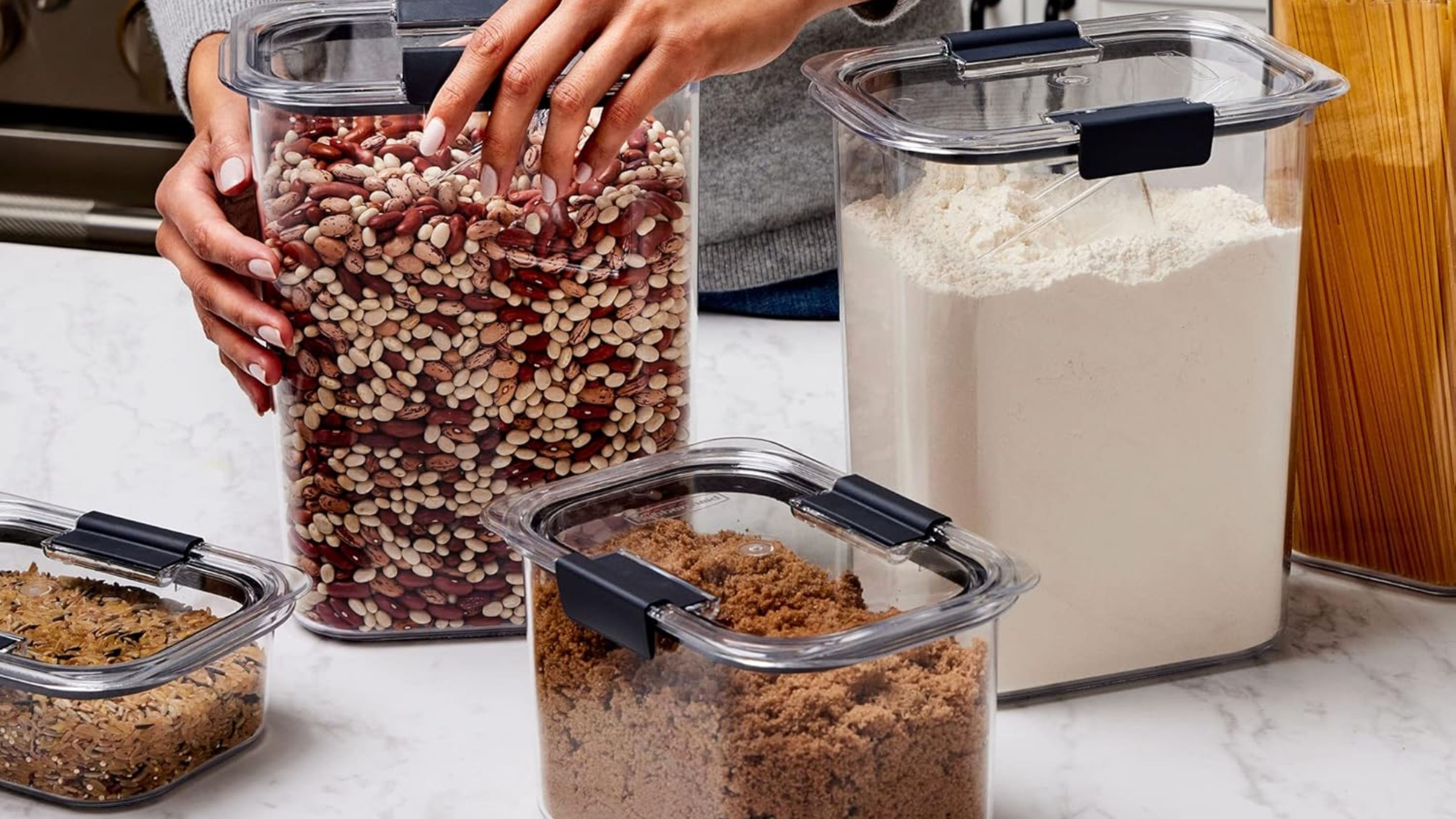 A set of Rubbermaid Brilliance containers on a marble kitchen counter filled with dried pantry goods