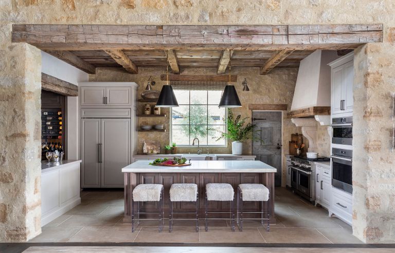 kitchen with white cabinets and island and exposed wooden rafters and stone walls