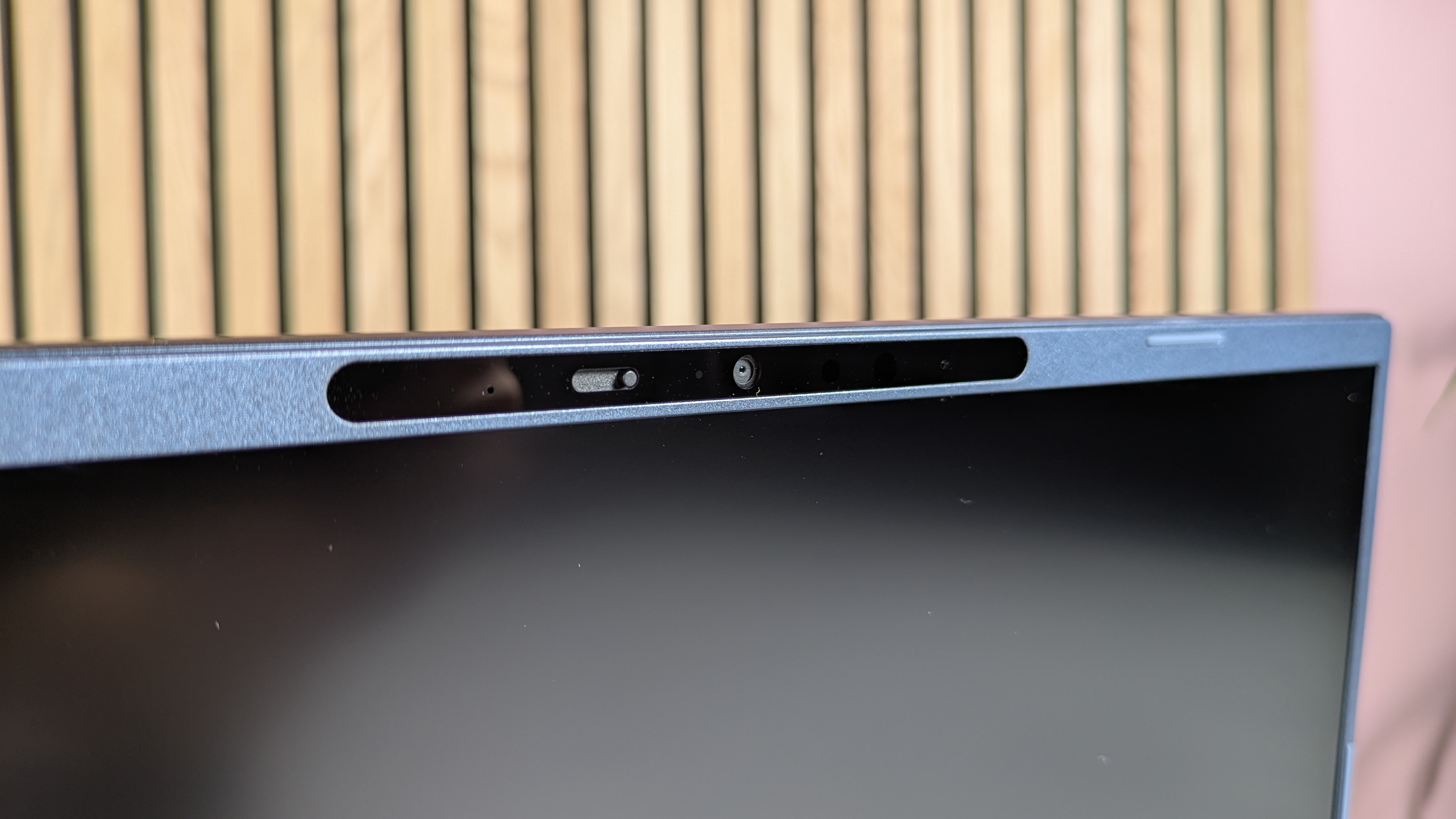 Close-up of webcam on Acer Aspire 14 AI (2025), open on desk with wooden panel, plant, and pink wall in background