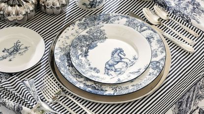 table set with striped tablecloth, silverware, and toile dinner plates