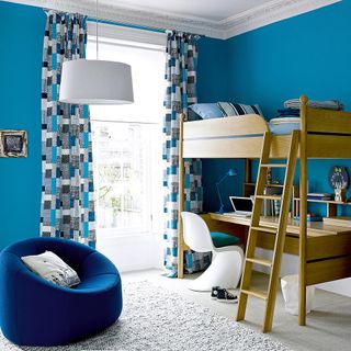 blue bedroom with patterned curtains and wooden bunk bed with desk area