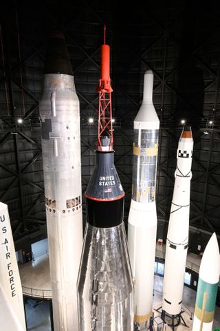 a large white and silver rocket stands upright in a large hangar