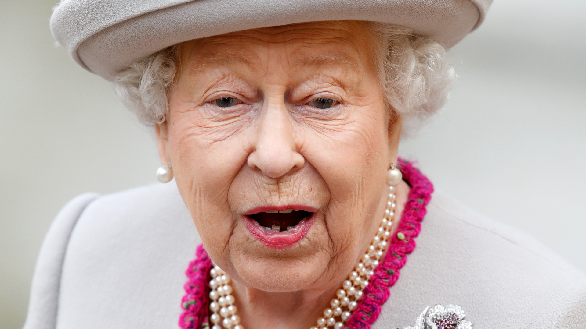 Queen Elizabeth looks shocked while wearing a gray and cerise coat and matching hat