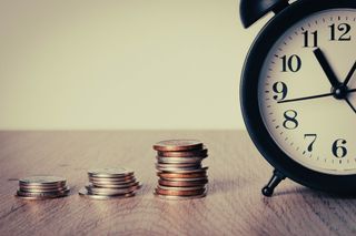 analog alarm clock set next to stacks of coins