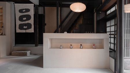 Image of a minimal boutique in Japan with an island counter and concrete floors. There is a stair area that has a pair of noren curtains hanging in the doorway.