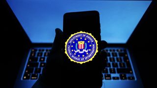 FBI logo on phone held in front of laptop with blue screen