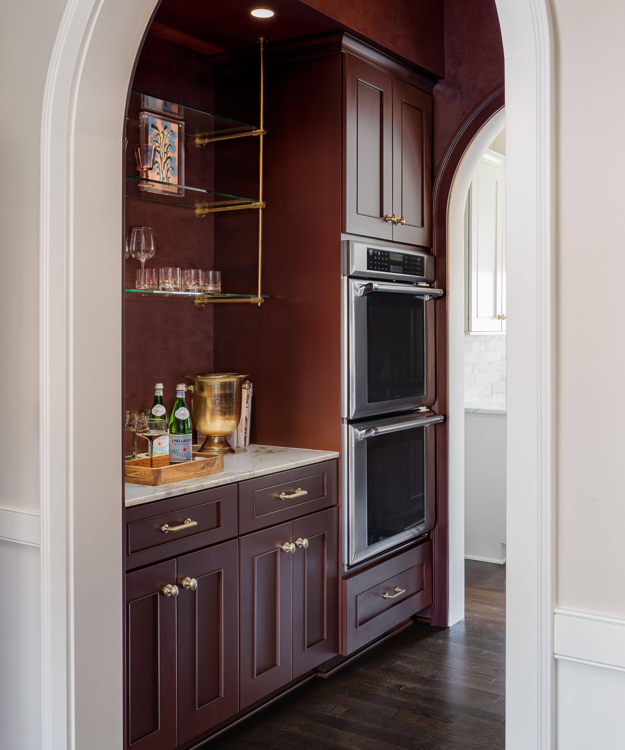 an arched doorway looks through to a dark red color drenched butlers pantry