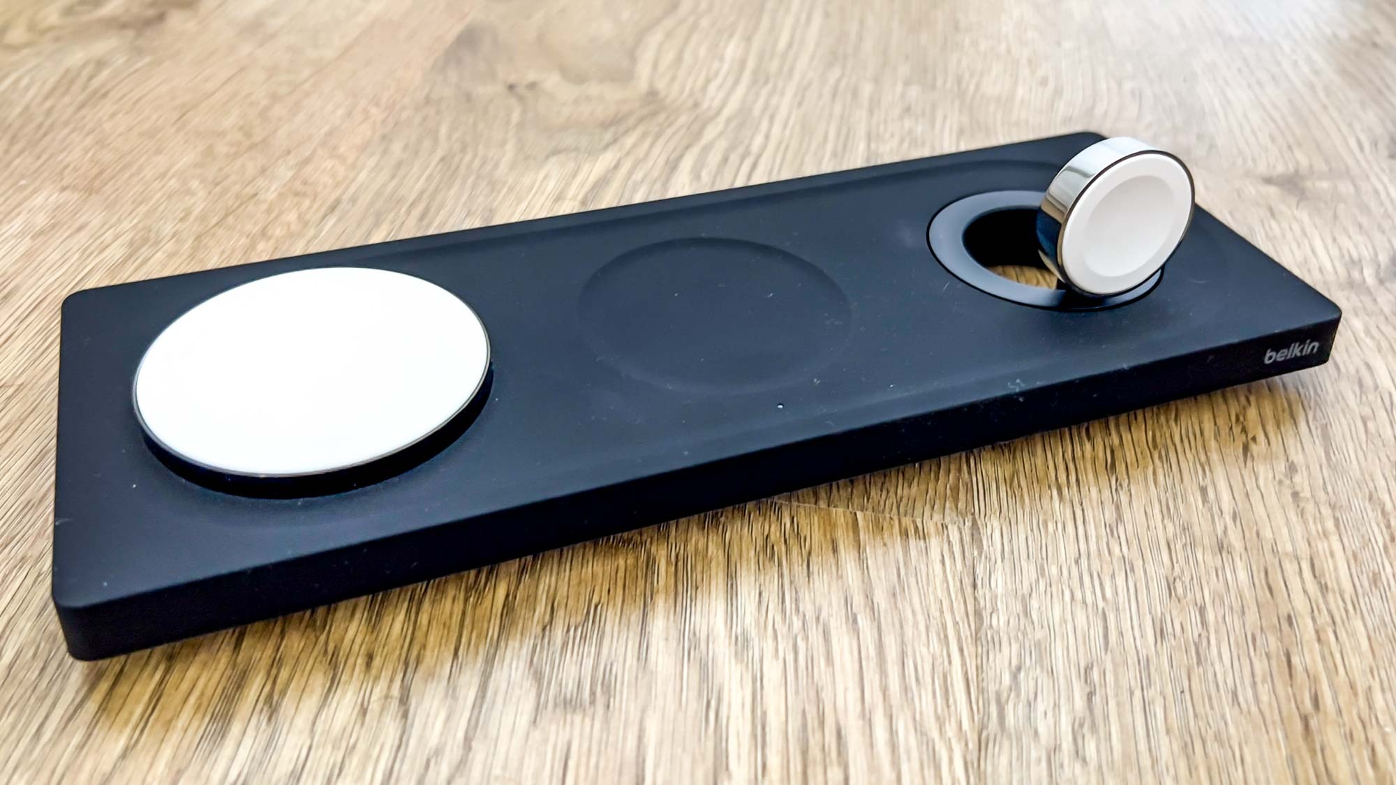 The Belkin BoostCharge Pro 3-in-1 Wireless Charging Pad with MagSafe in black on a wooden surface