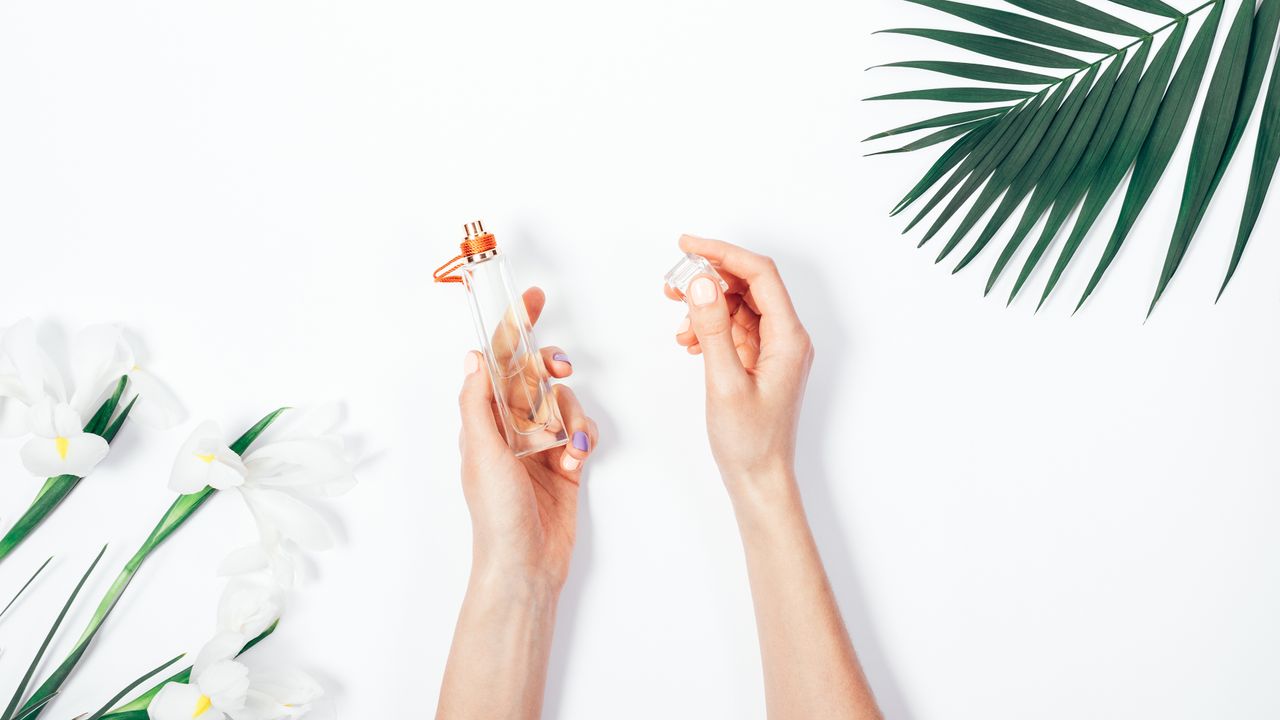 Hands taking the lid off one of the best women&#039;s perfumes against a white background with green flowers and leaves