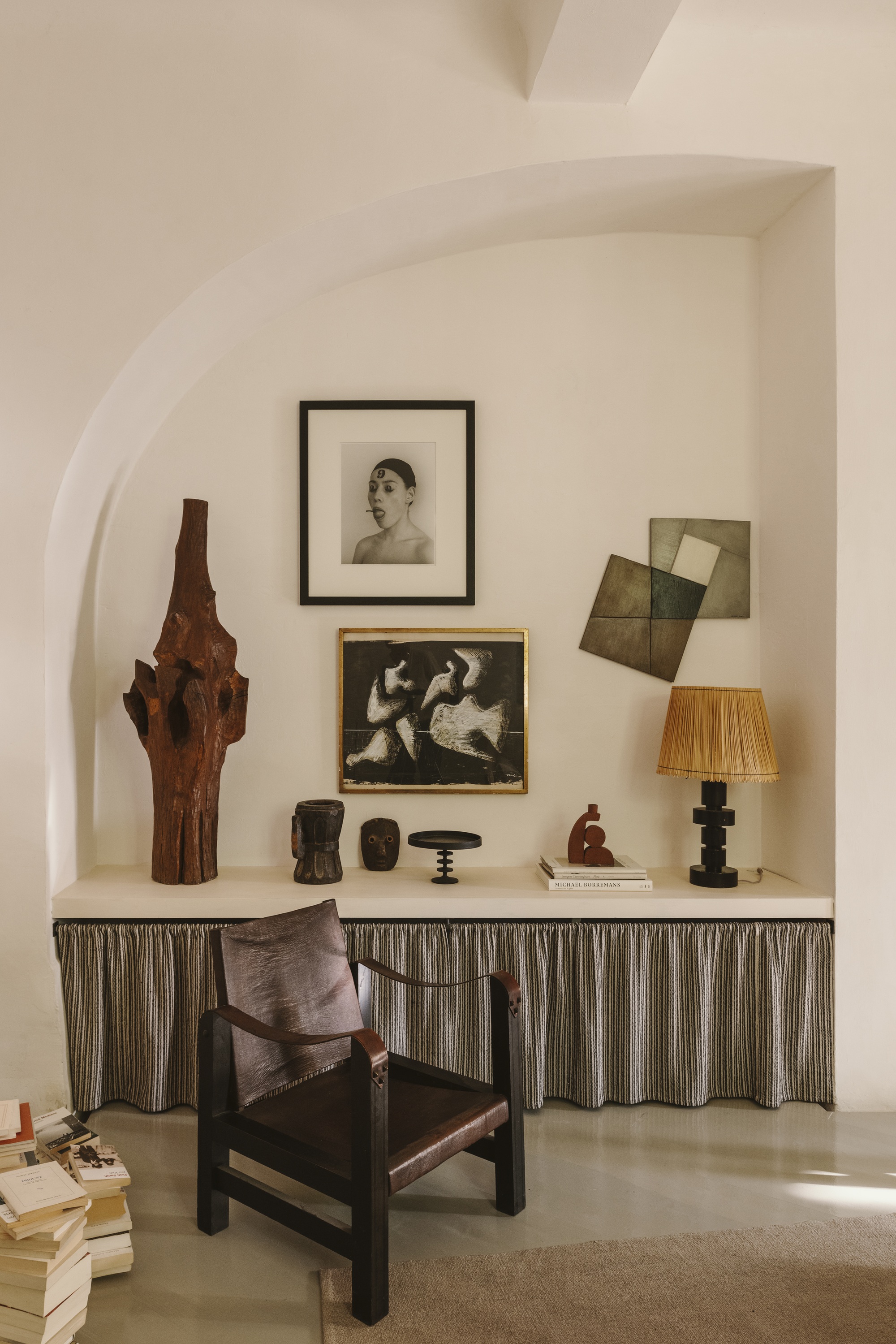 a neutral living room with a shelf with a striped skirt underneath. there are modern rustic objects on the shelf and artwork